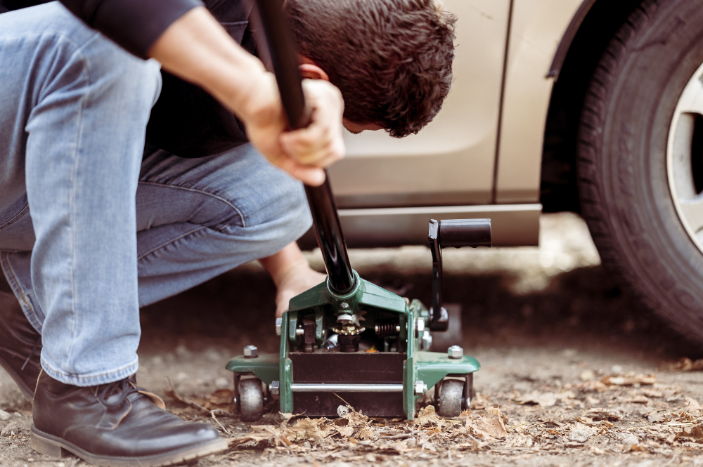 Muškarac koristi hidrauličnu dizalicu za podizanje automobila. Kleči na podu i koncentrira se na rukovanje dizalicom.